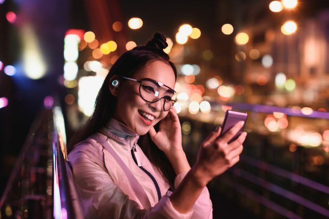 onnellinen aasialainen tyttö, jolla on videokeskustelu älypuhelimella ja kuulokkeilla